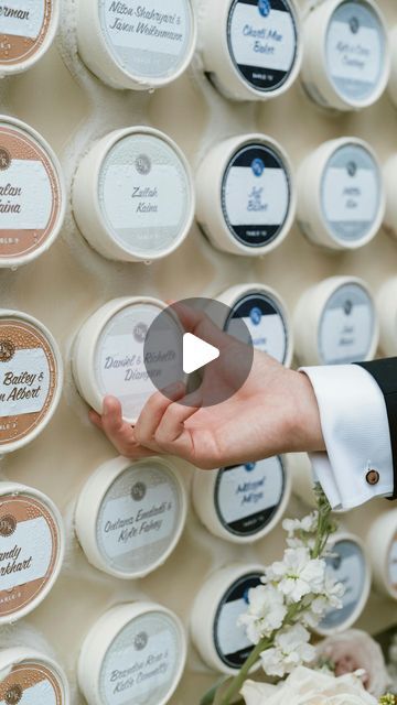 a person holding out their hand in front of a wall full of round jars with labels on them