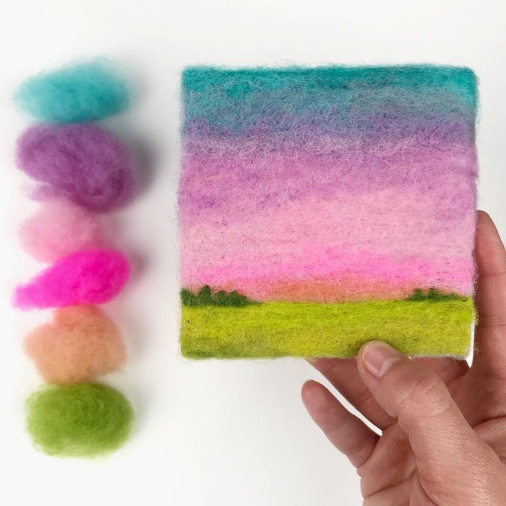 a hand holding a small piece of felt with different colors on it next to some yarn balls