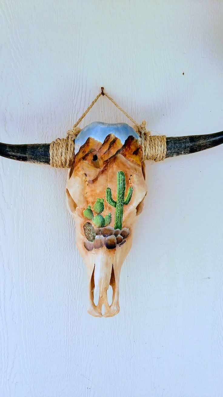 a cow skull hanging on the side of a wall with a cactus and mountains painted on it