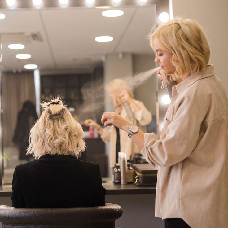 a woman is getting her hair done in front of a mirror and another person sitting at the counter