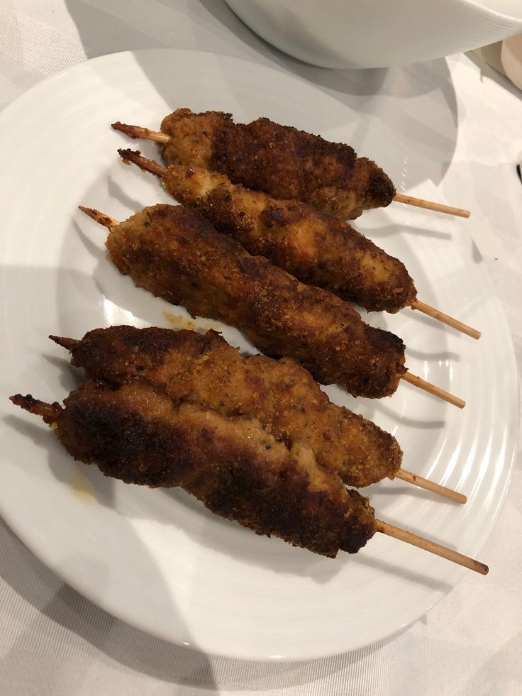 three chicken skewers on a white plate next to a cup and saucer