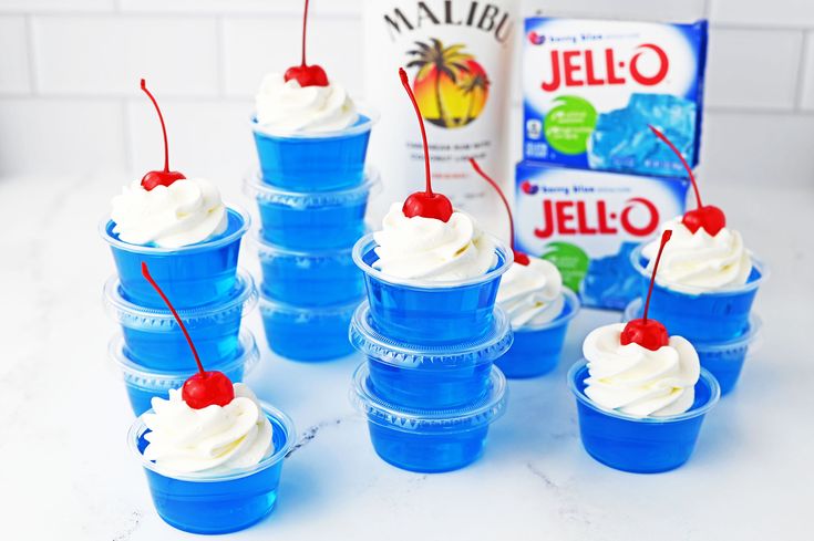 blue cups filled with whipped cream and cherries next to a carton of jello