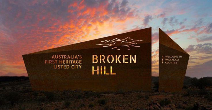 there is a sign that says broken hill in front of the sun setting behind it