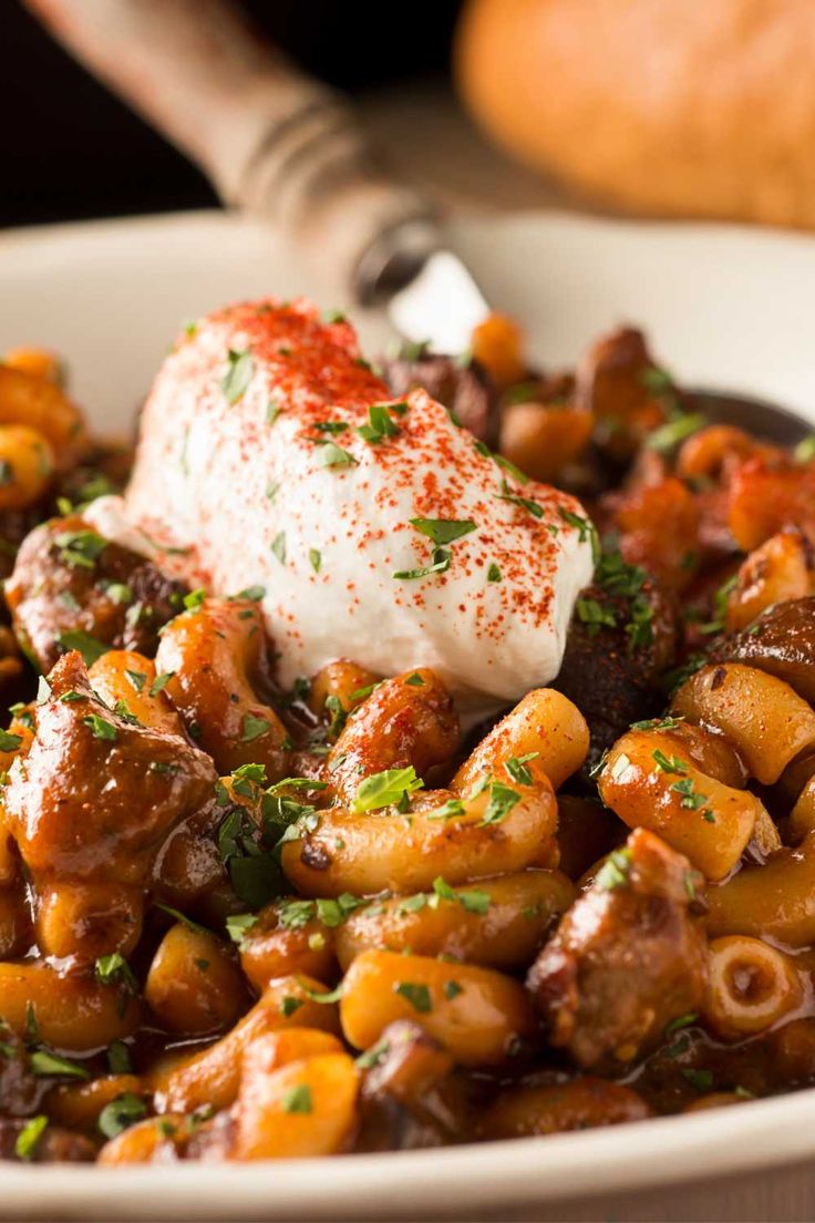 a white bowl filled with pasta and meat covered in sauce, garnished with parsley