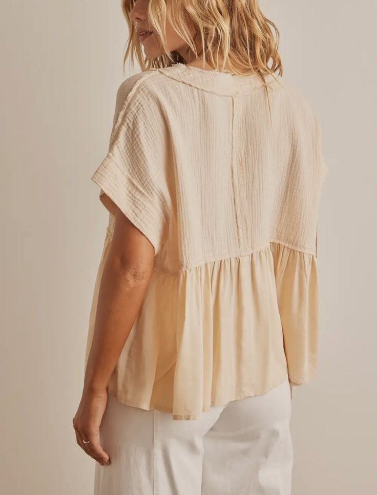 a woman in white pants and a beige top is looking down at the back of her shirt