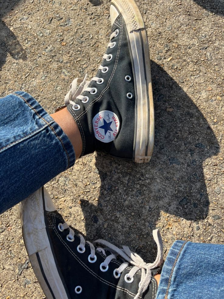 someone's feet wearing converse shoes on the ground