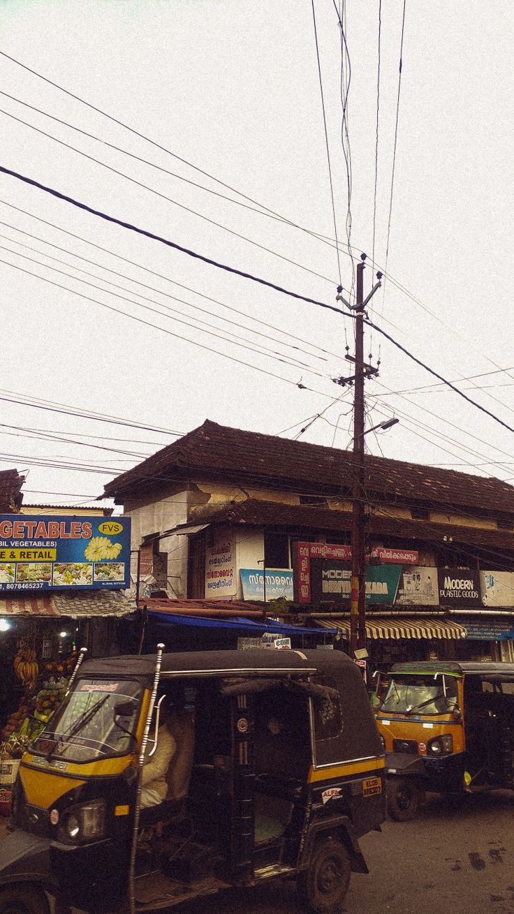 two tuk tuks parked in front of a small building on the street with power lines above them