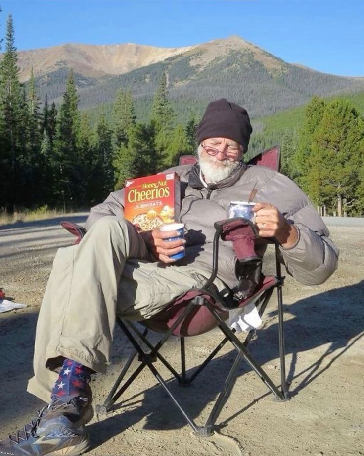 an old man sitting in a chair holding a box of cheetos