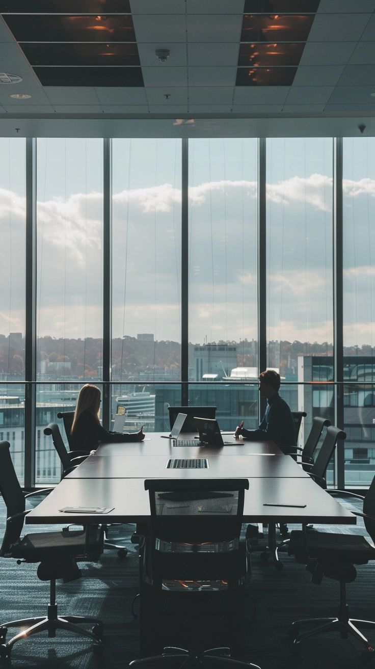 two people sitting at a conference table in front of large windows