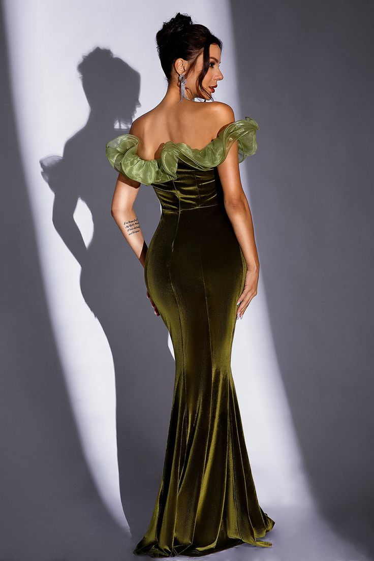 a woman in a long green dress standing next to a white wall with her shadow on it