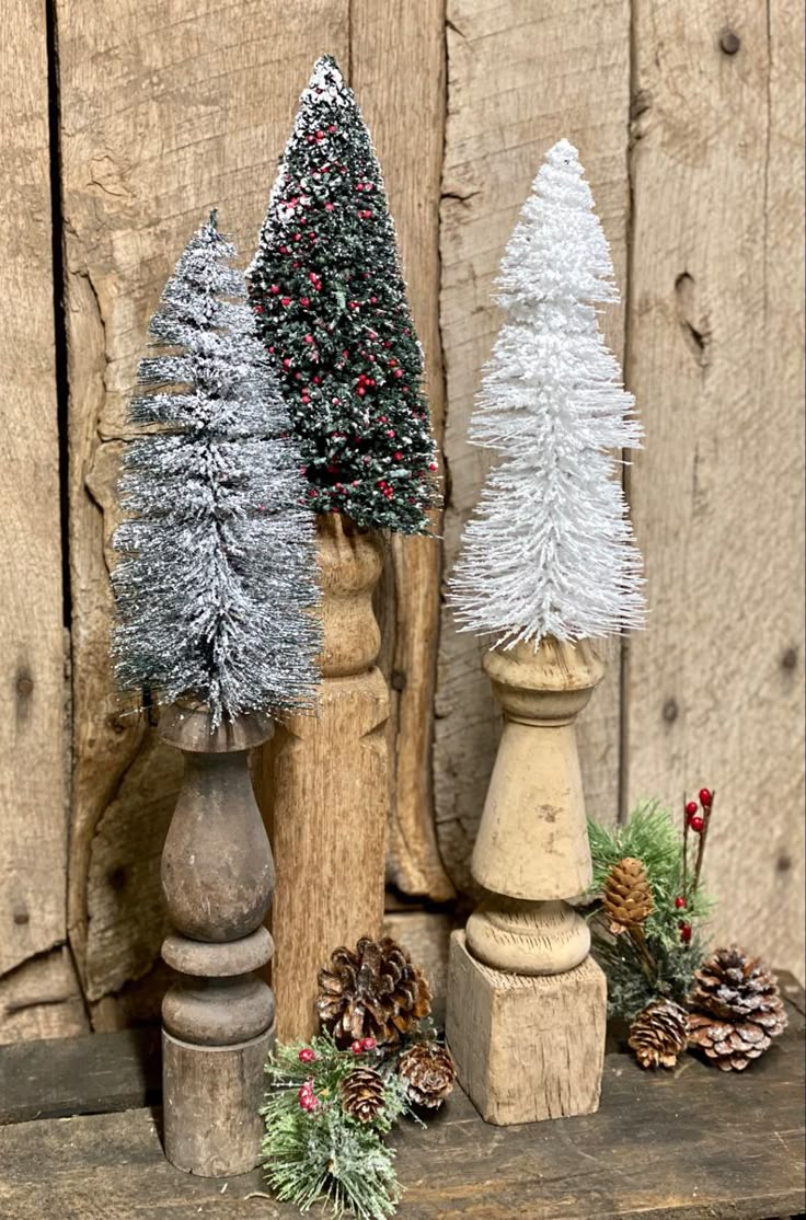 three small christmas trees sitting on top of wooden posts next to pine cones and berries