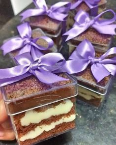 there are several desserts with purple ribbons in the box on the table and someone holding one