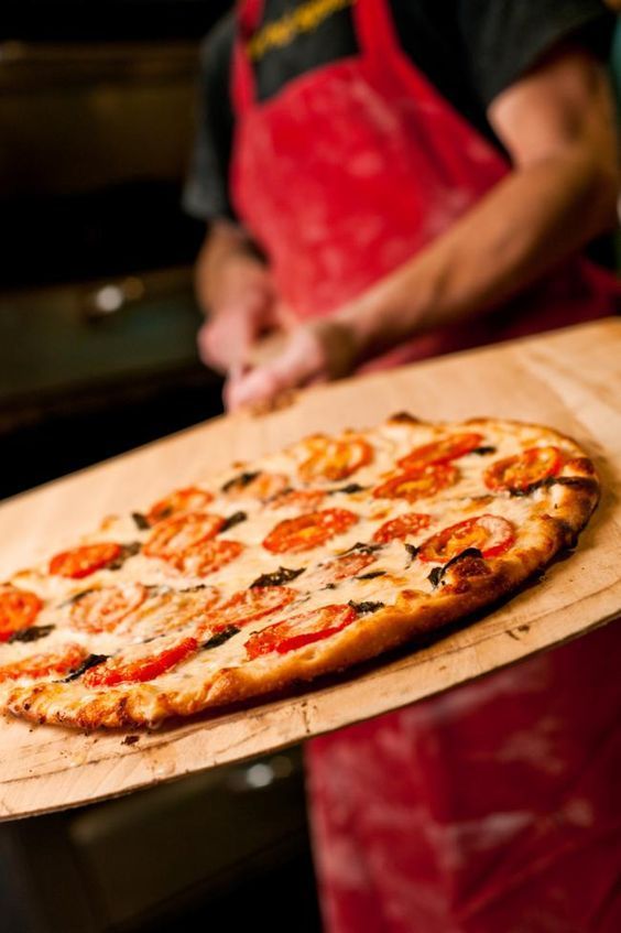 a pizza sitting on top of a wooden cutting board next to a person in an apron