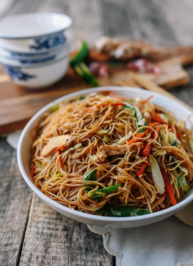 a bowl filled with noodles and vegetables on top of a wooden table next to chopsticks