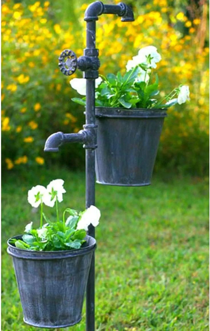 two potted plants are attached to a water faucet in the grass with yellow flowers behind them