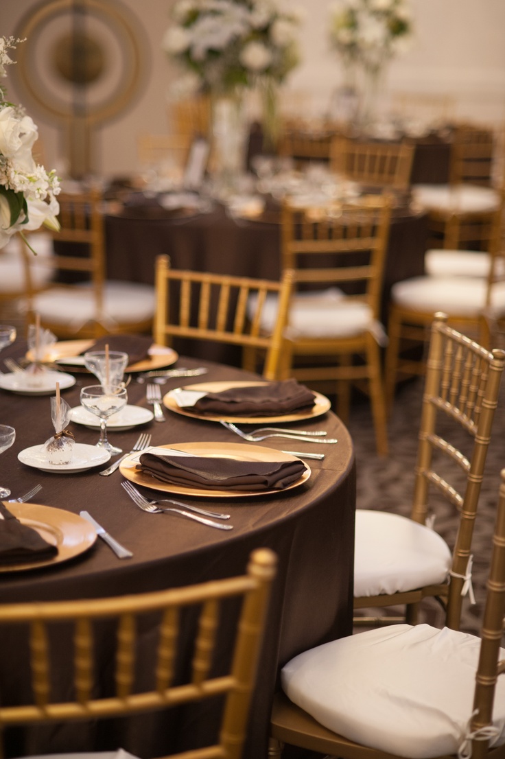 the table is set with gold chairs and white flowers