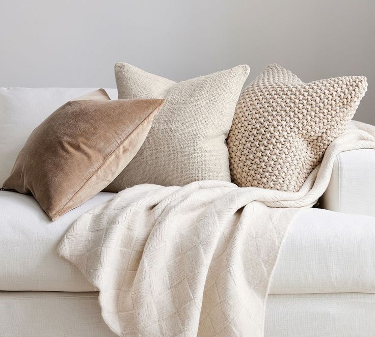 a white couch with pillows on top of it and a blanket draped over the back