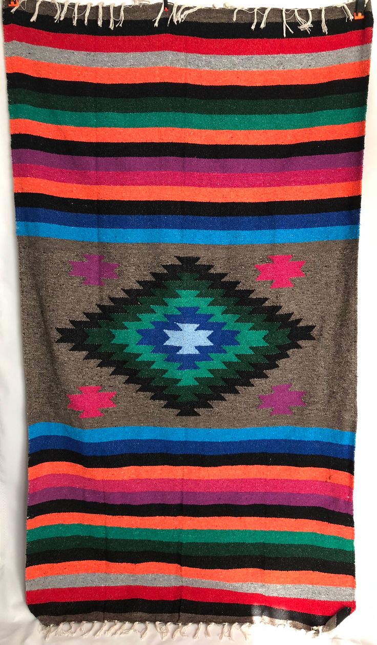 a multicolored blanket with fringes hanging from the side on a white wall