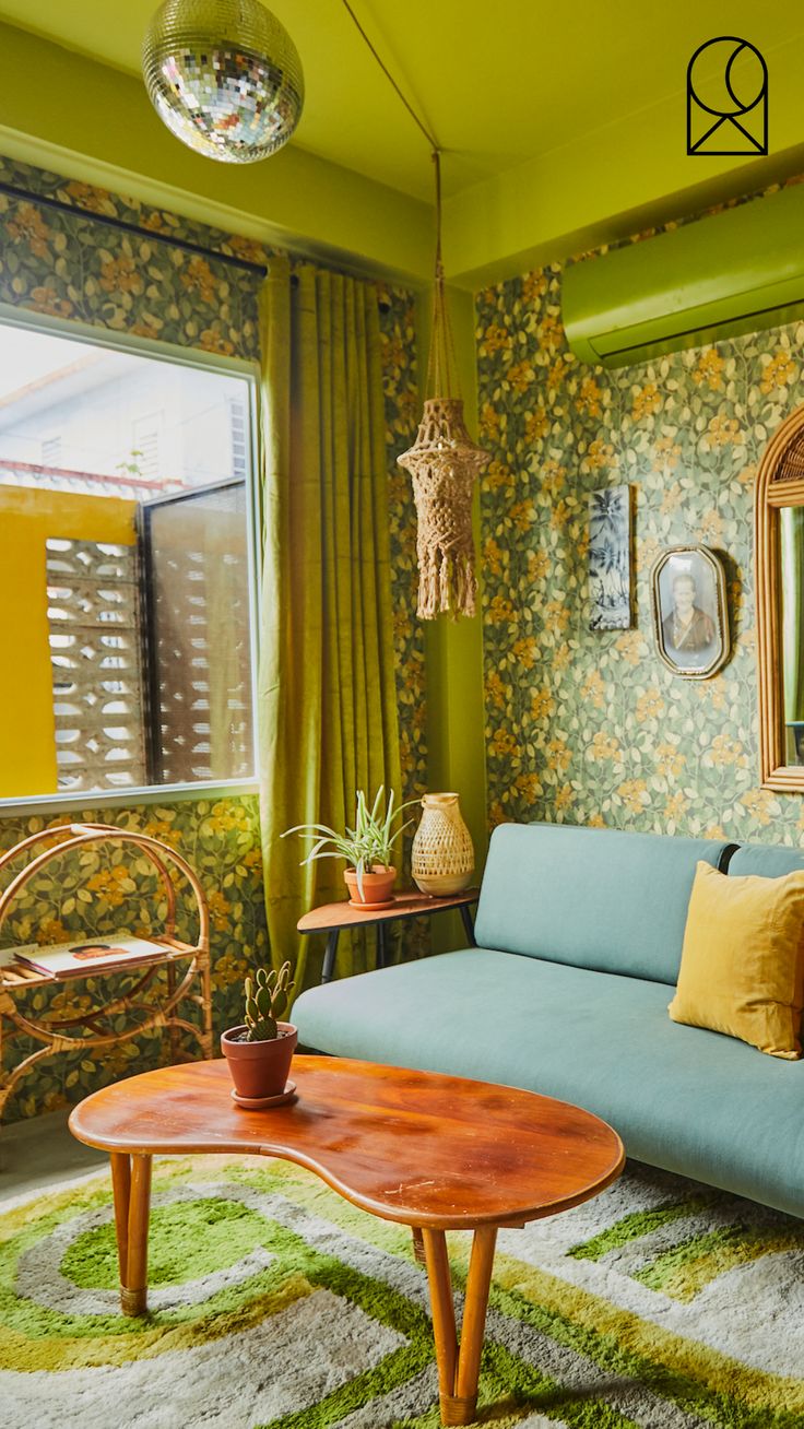 a living room with green walls and floral wallpaper on the walls, a blue couch in front of a round coffee table