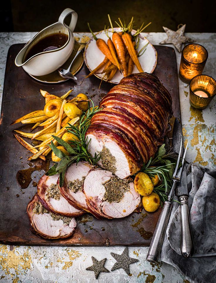 a platter with sliced ham, potatoes and carrots on it next to silverware