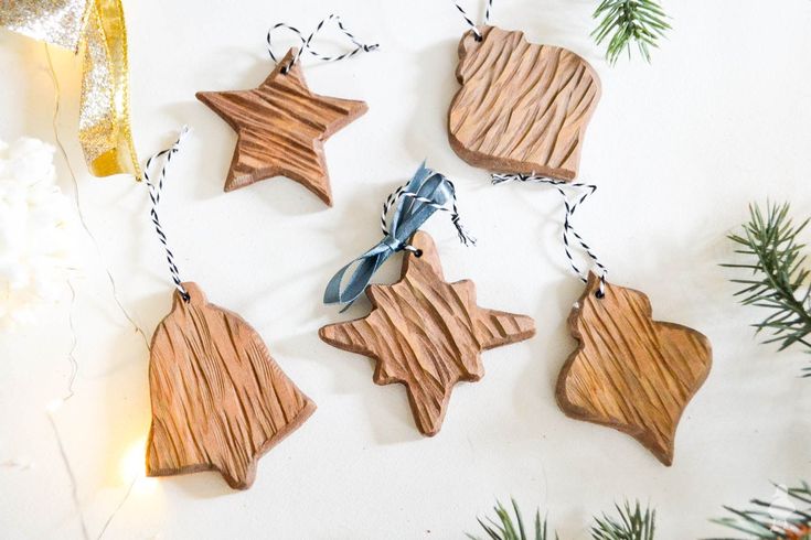 three wooden ornaments hanging from strings on a white surface with pine branches and snowflakes