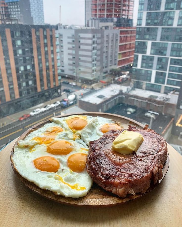 two eggs and steak are on a plate in front of a cityscape with skyscrapers