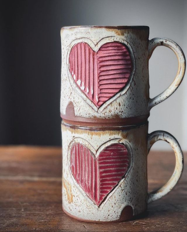 two coffee mugs with hearts painted on them sitting on a wooden table top together