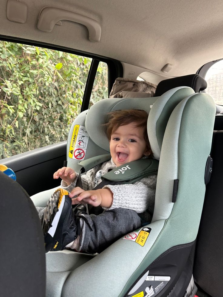 a small child sitting in a car seat with his mouth open and tongue hanging out