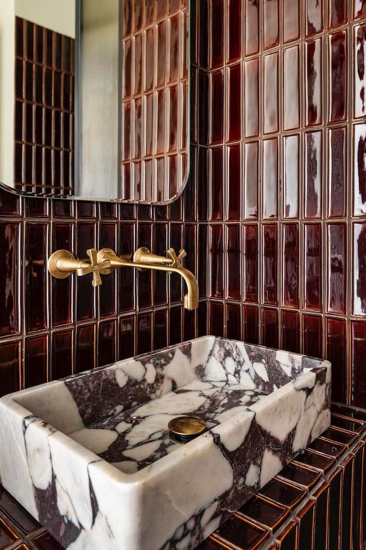 a marble sink with gold faucet in front of a brown and white tiled wall