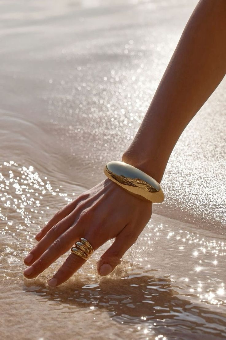 a person's hand reaching for something in the water at the beach with sunlight shining on them