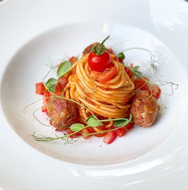 a white plate topped with spaghetti and meatballs covered in tomato sauce, garnished with green leaves