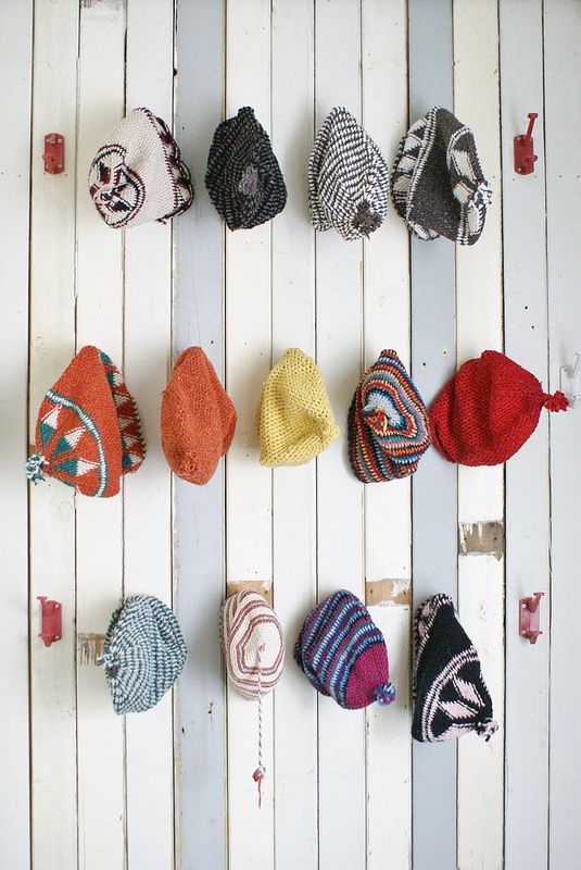 several different types of hats hanging on a white wooden wall with pins attached to them