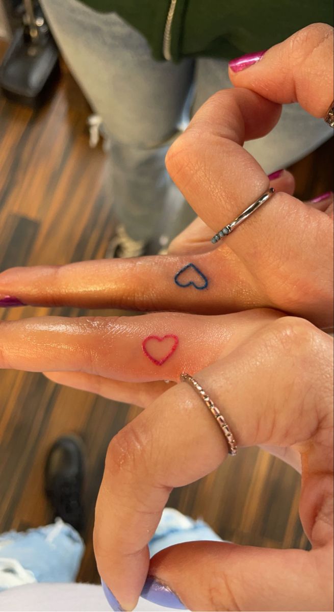 two fingers with hearts tattooed on them, one is pink and the other is blue