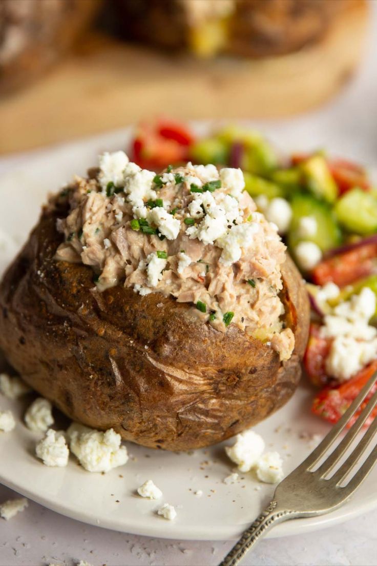 a white plate topped with a baked potato covered in feta cheese next to a salad