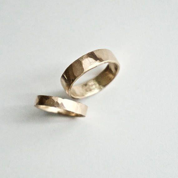 two gold wedding bands sitting on top of a white surface with one ring in the middle