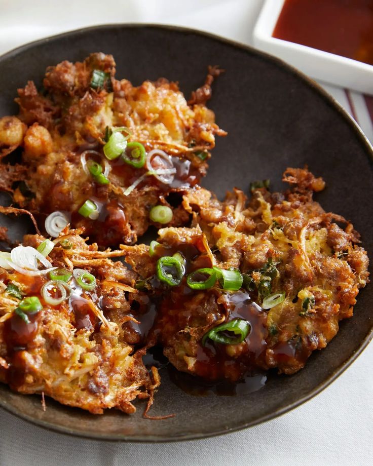 three fried food items on a plate with sauce and seasoning next to it, ready to be eaten