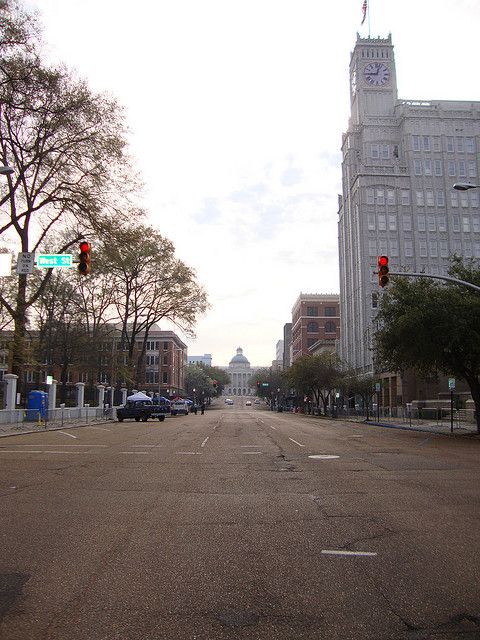 an empty street with cars parked on both sides and tall buildings in the back ground