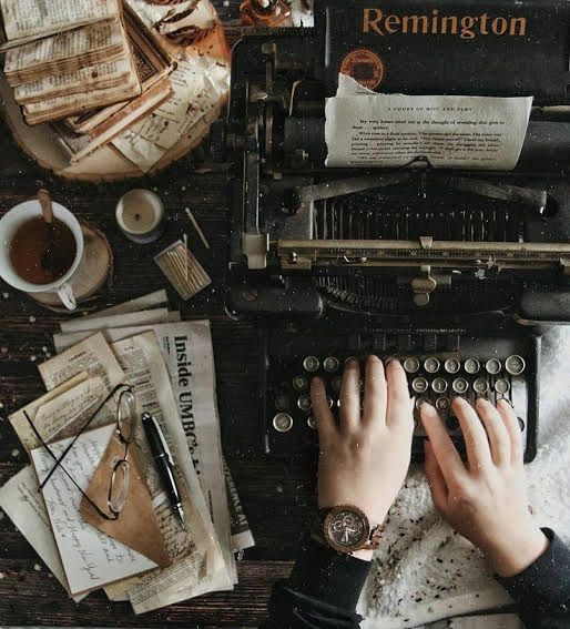 a person typing on an old typewriter surrounded by papers and other things that are scattered around