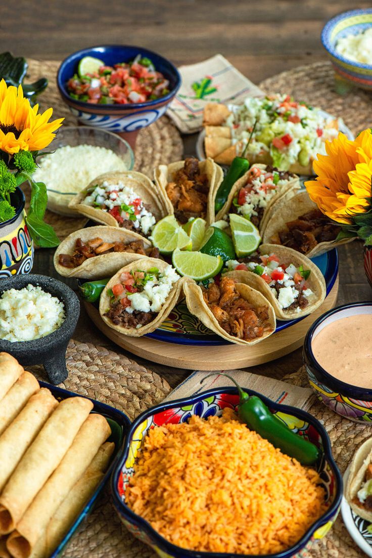 mexican food is laid out on a table with sunflowers and other foods in bowls