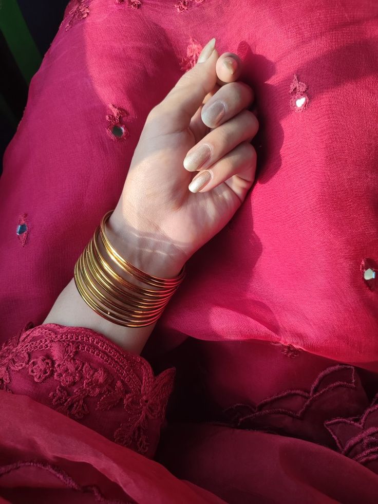 a woman's hand resting on top of a pink pillow with gold bracelets