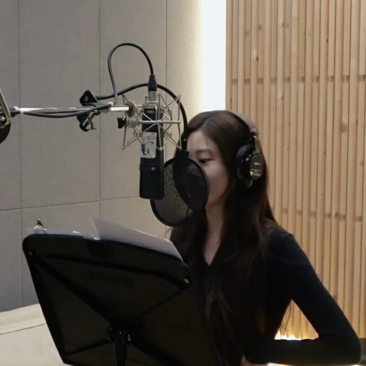 a woman sitting in front of a microphone with headphones on and looking at her laptop