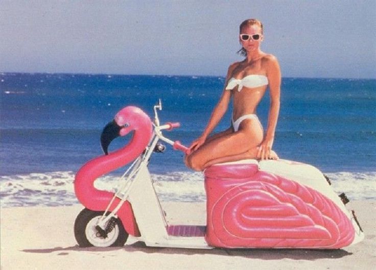 a woman sitting on top of a pink flamingo scooter at the beach