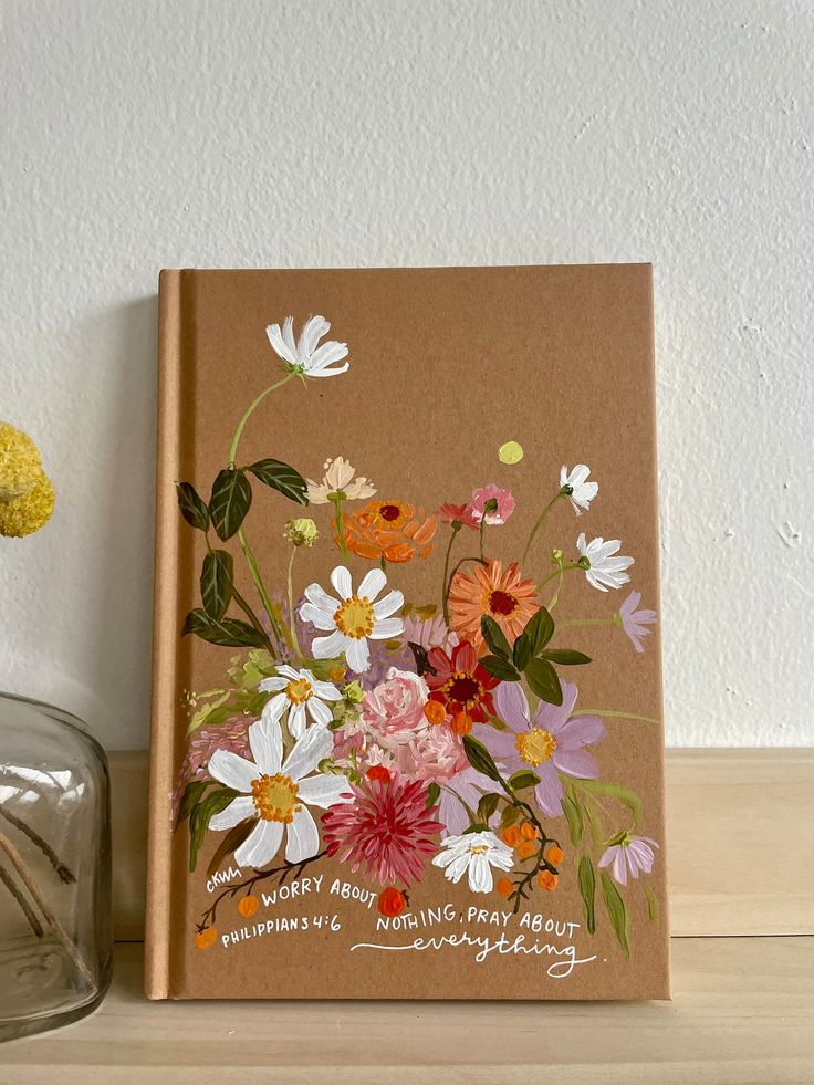 a book sitting on top of a wooden table next to a vase filled with flowers