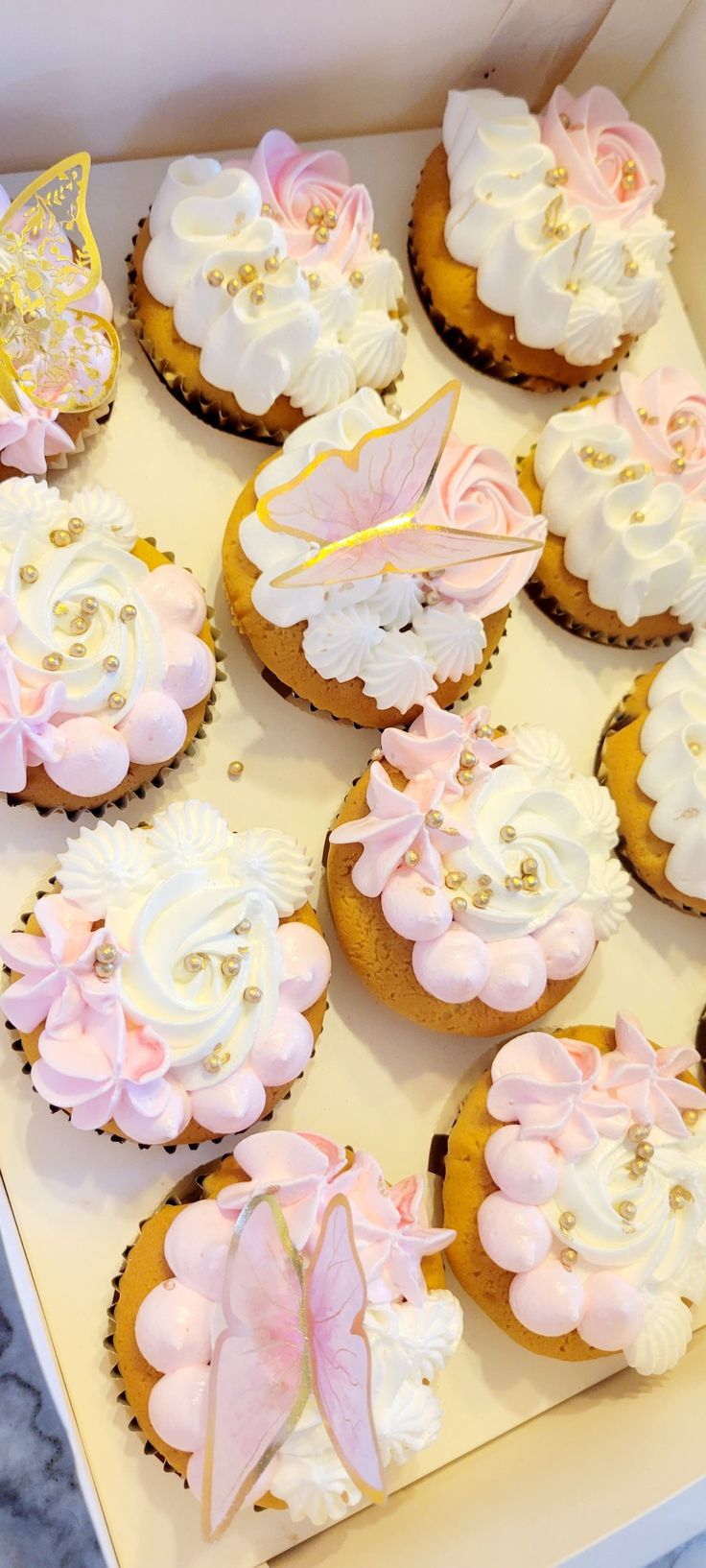 a box filled with lots of cupcakes covered in frosting and pink icing