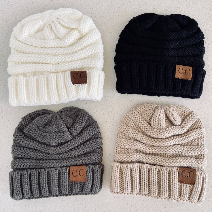 three knit beanies with leather tags on them are lined up against a white background