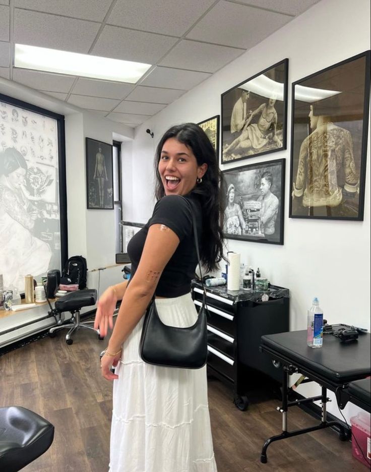 a woman standing in a hair salon holding a black purse and smiling at the camera