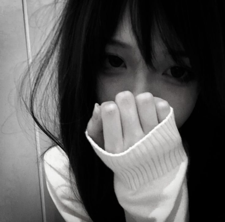 black and white photograph of a woman covering her face with her hand while standing in front of a wall