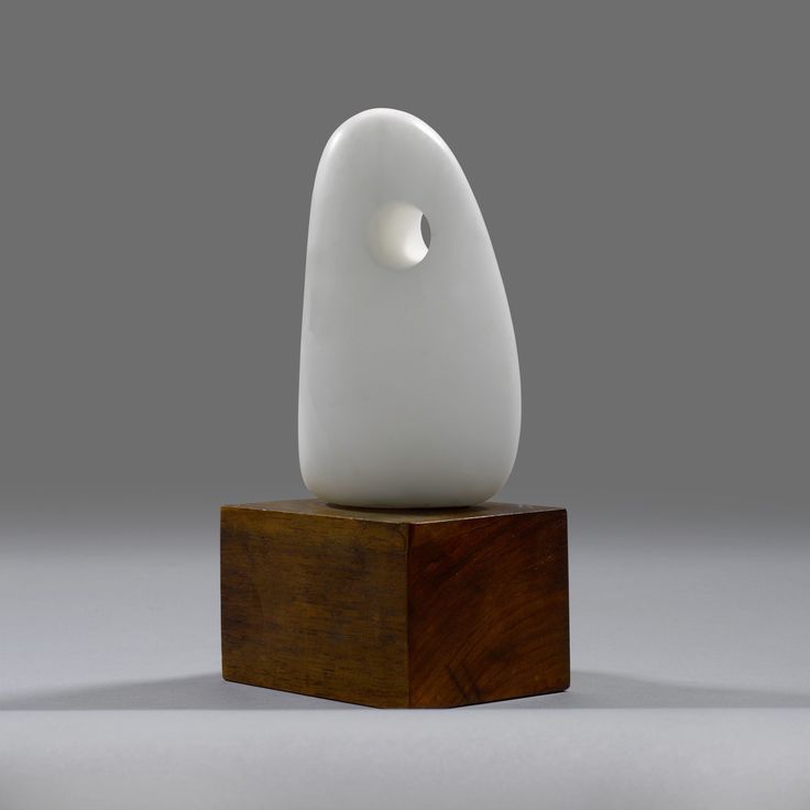 a white sculpture sitting on top of a wooden block in front of a gray background