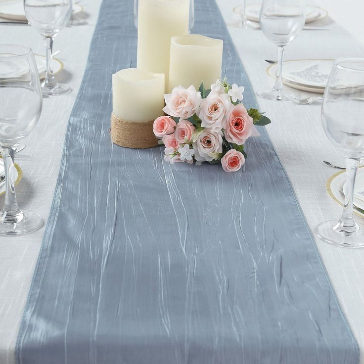 a table topped with candles and flowers on top of a blue table cloth next to wine glasses