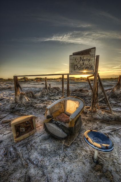 an old chair sitting on top of a sandy beach next to a broken down sign